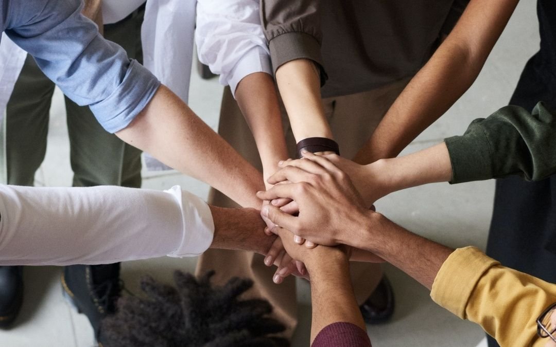 eight hands of various skin tones held together showing arms like spokes of a wheel